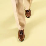 Timothée Paris handcrafted cognac brown leather apron-toe mocassin shoes with dark lacing and black rubber sole, worn in motion with beige trousers on a lime green surface — men's luxury shoes made in Portugal
