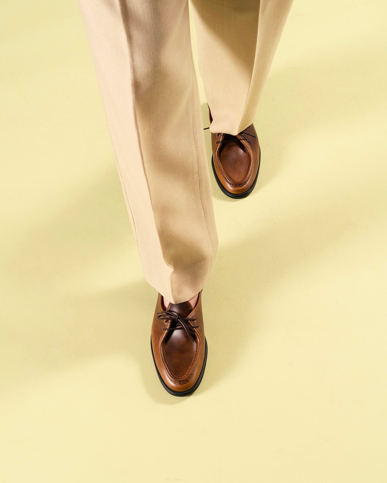Timothée Paris handcrafted cognac brown leather apron-toe mocassin shoes with dark lacing and black rubber sole, worn in motion with beige trousers on a lime green surface — men's luxury shoes made in Portugal