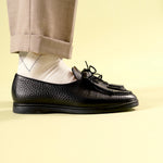 Person wearing black Beaune loafer mocassin shoes with rubber sole and white argyle socks on a light yellow background side view