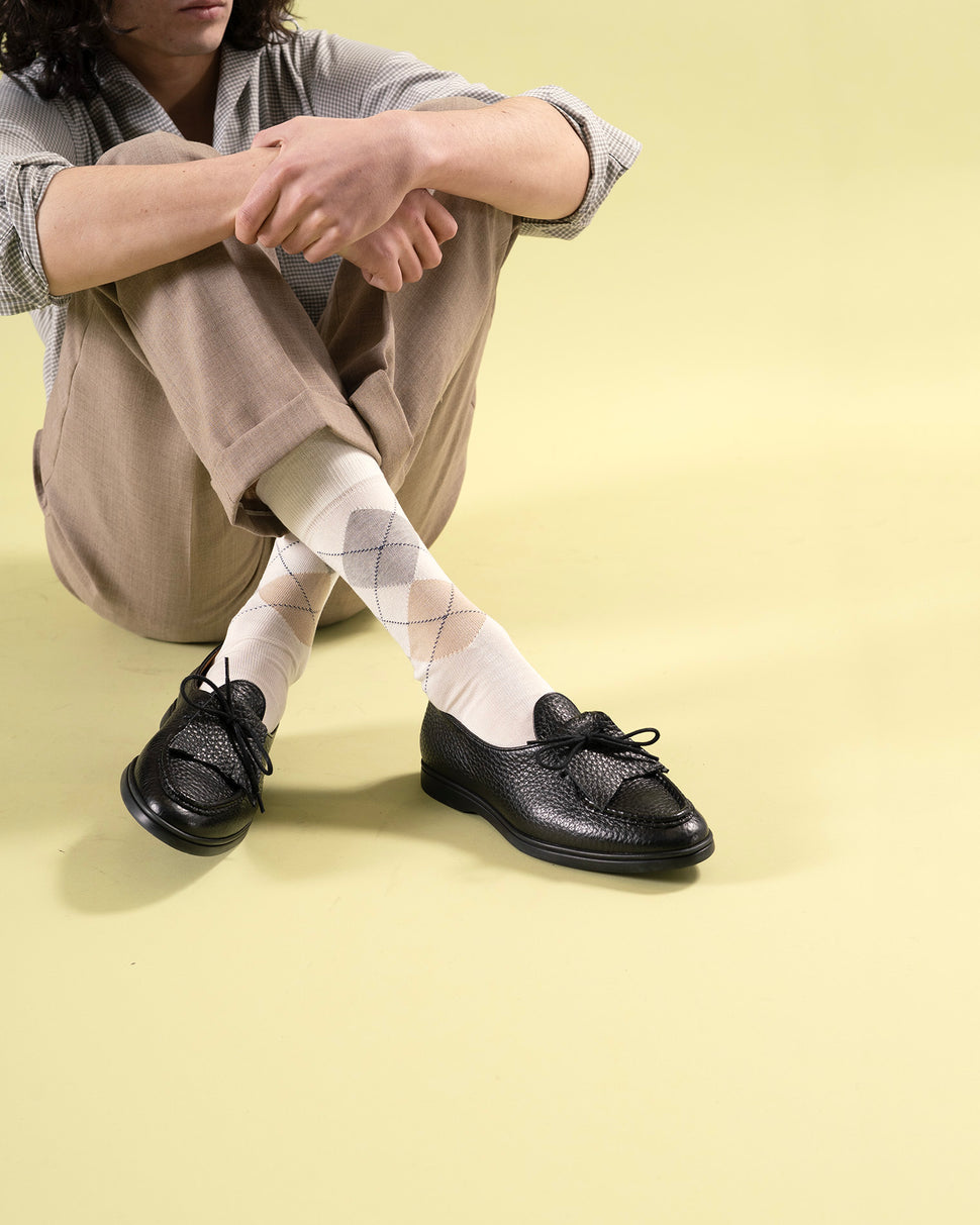 Person wearing black Beaune loafer mocassin shoes with rubber sole and white argyle socks on a light yellow background
