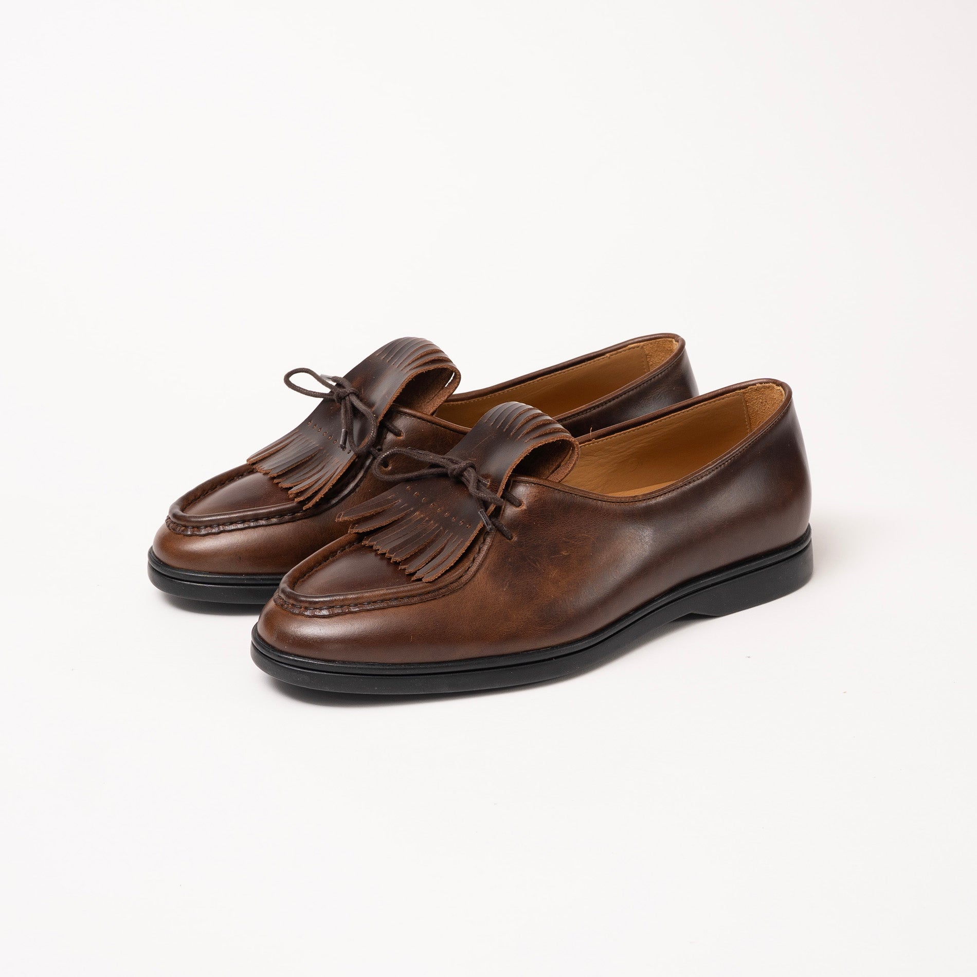 Pair of brown loafers with fringes by Timothée Paris on a white background