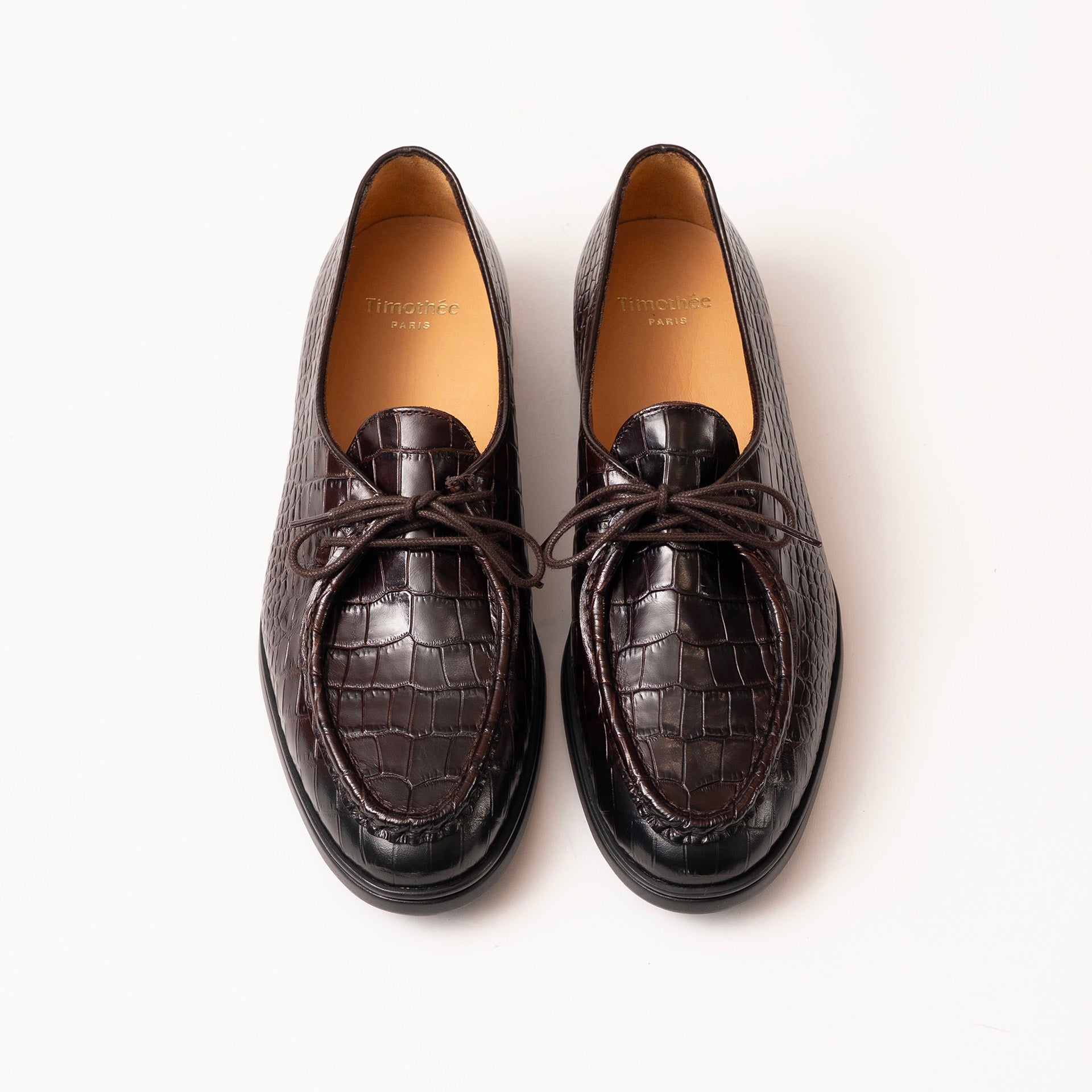 A pair of burgundy crocodile-embossed leather loafer by Timothée Paris with matching laces, shown from a top-down view on a clean white background.