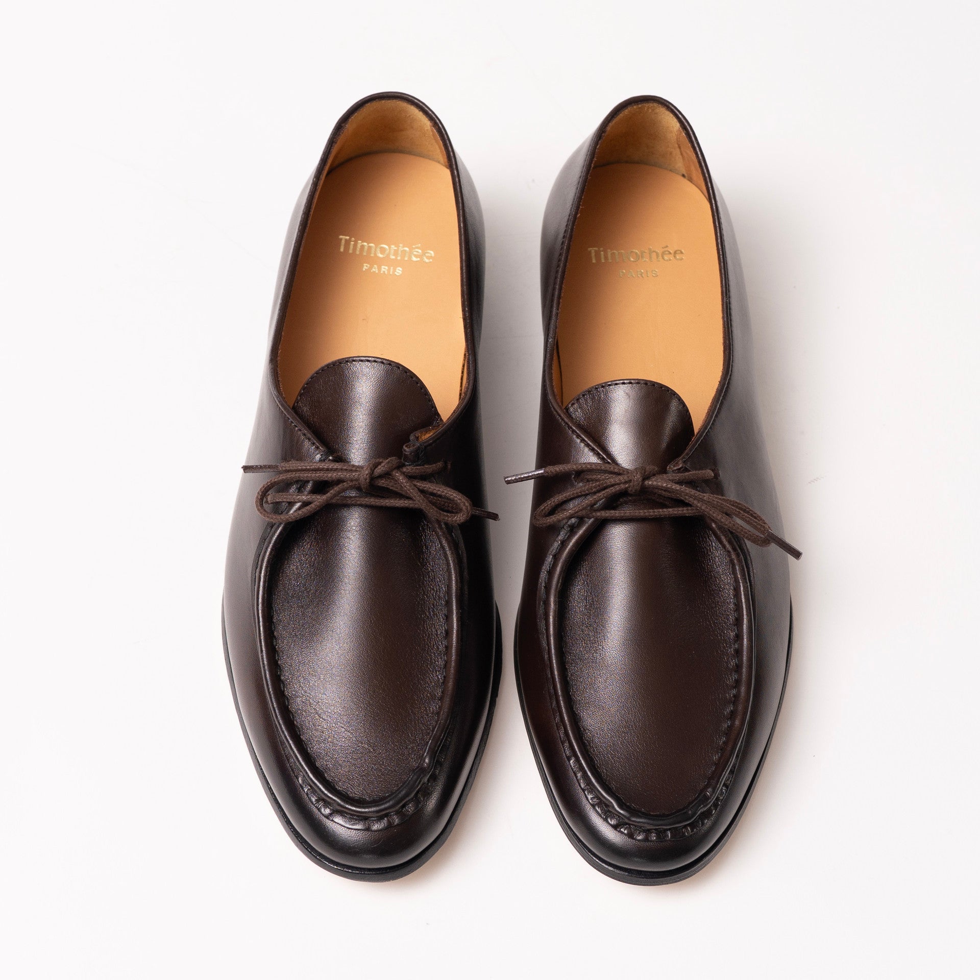 A pair of dark brown leather loafers with  laces, shown from a top-down view on a clean white background. The brand name 'Timothée PARIS' is visible on the tan insoles.
