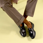 Timothée Paris black leather moccasin derby shoes Beaune with apron toe, worn with dark brown wide-leg trousers and cognac orange socks against a lime green background