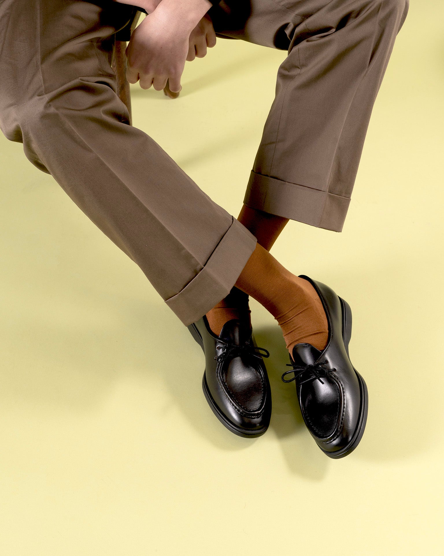 Timothée Paris black leather moccasin derby shoes Beaune with apron toe, worn with dark brown wide-leg trousers and cognac orange socks against a lime green background