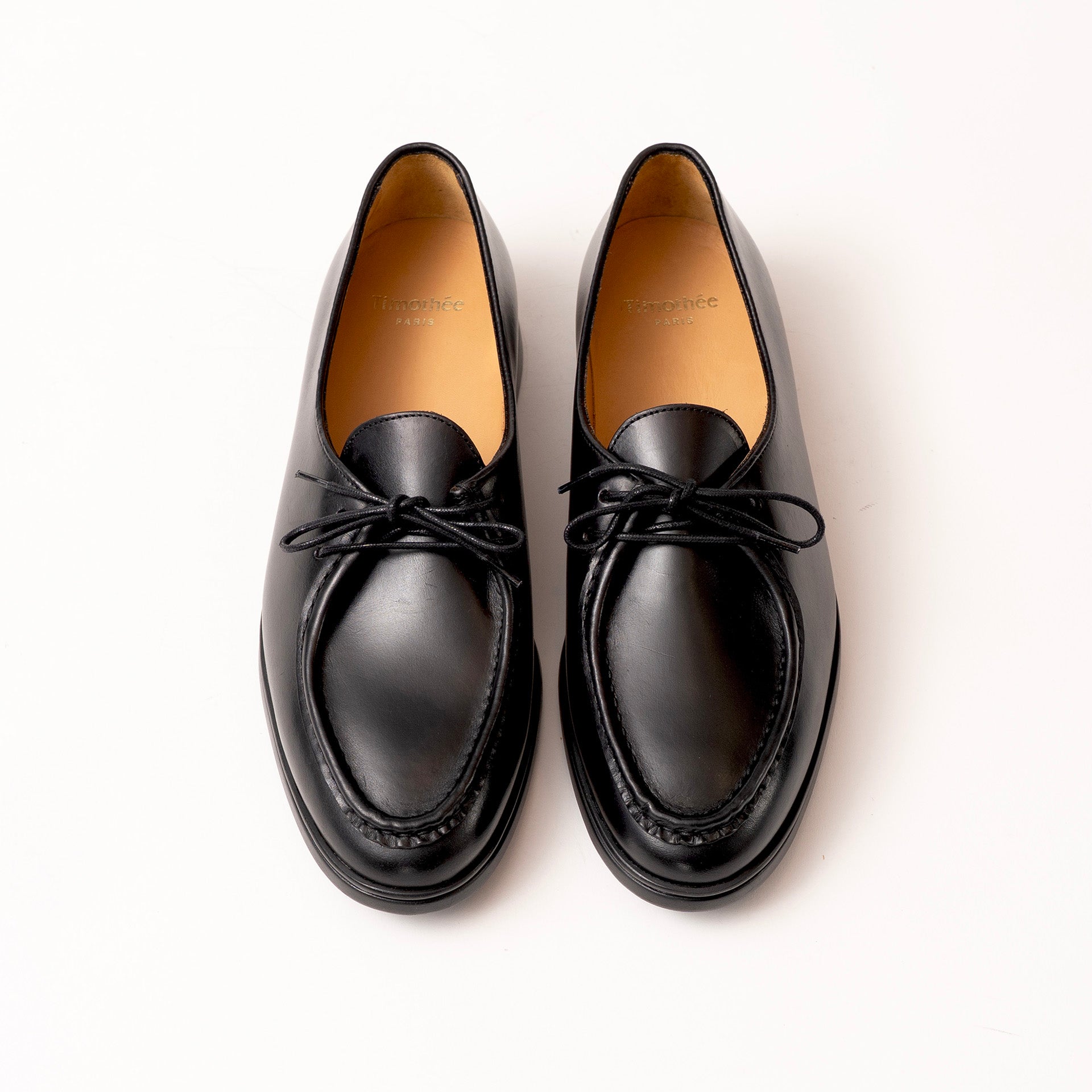 A pair of black leather loafers with moc toe and matching black laces by Timothée Paris, photographed from a top-down angle on a clean white background.