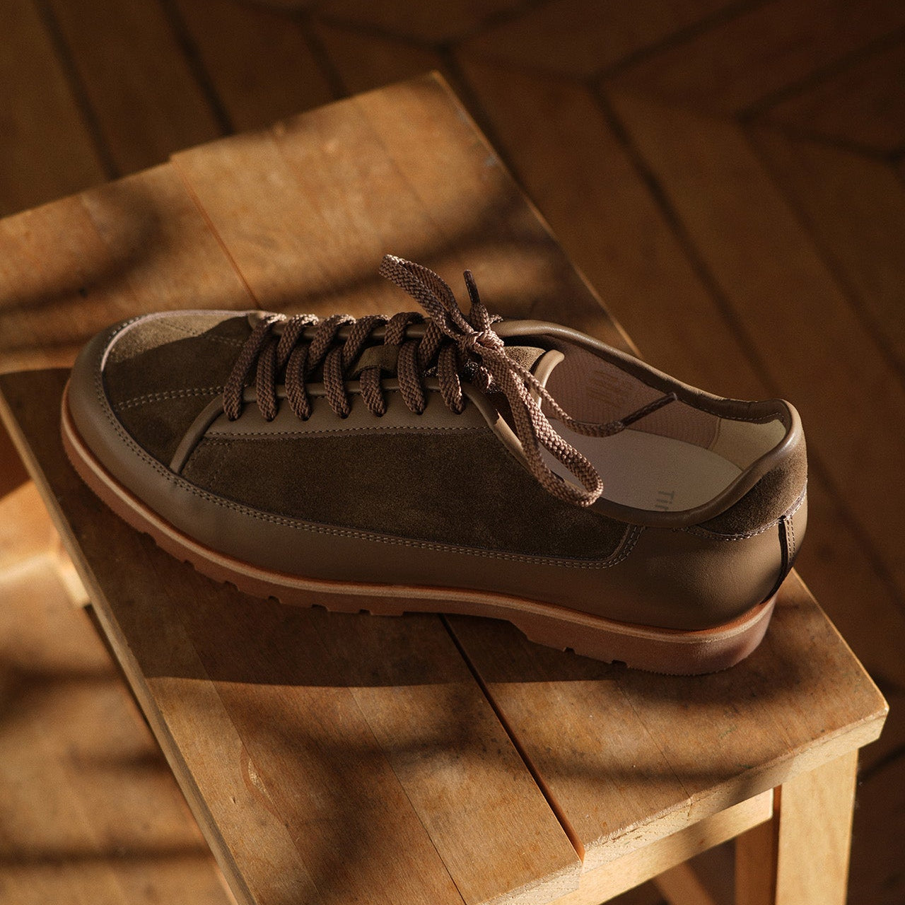 Brown suede and leather shoe Yport by Timothée Paris on a wooden stool with a warm, wooden background
