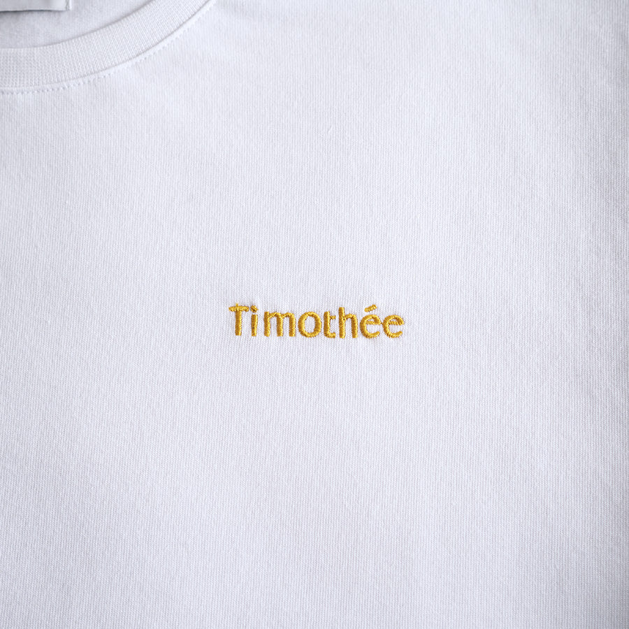 white-short-sleeve-embroidered-timothee-paris-logo-on-chest-oversized-tshirt-close-up-honey-gold